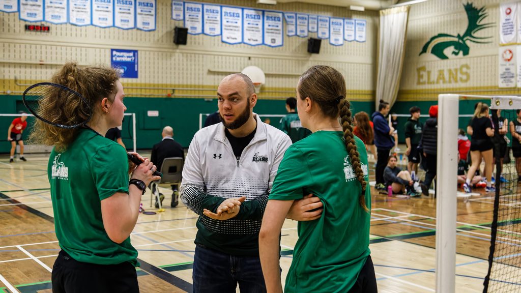 Deux étudiantes-athlètes  en badminton du cégep Garneau discutant avec leur entraîneur sur le terrain de badminton. 