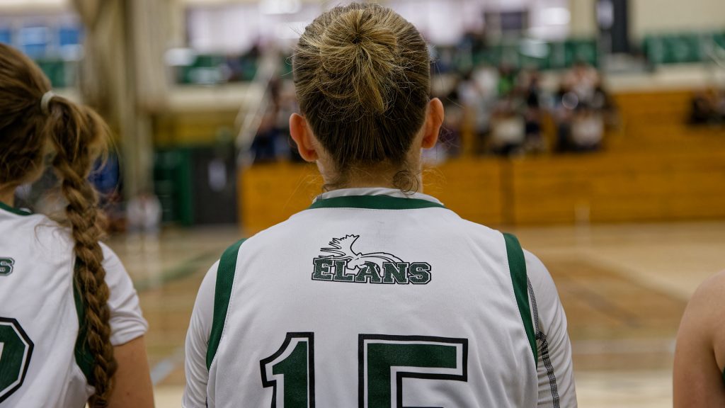 Athlète de l'équipe de basketball féminin 2e division du Cégep Garneau, Les Élans, assise sur le banc, vue de dos.